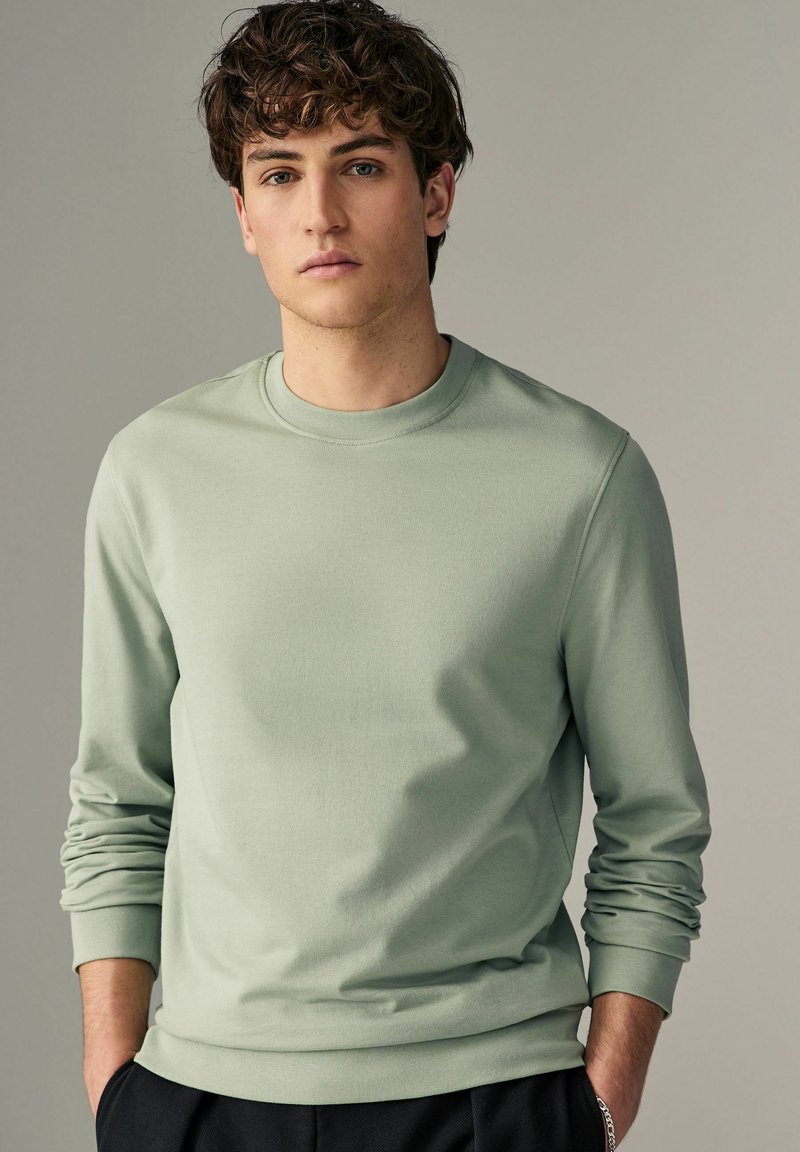 Sudadera verde claro hecha de tela suave, con cuello redondo, mangas largas y puños acanalados. Textura suave con detalles mínimos.