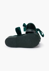 Zielone welurowe buty z okrągłym noskiem, wyposażone w materiałowe wstążki z tyłu i czarną gumową podeszwą, z widocznymi detalami tekstury na podeszwie.