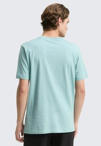 Svjetloplavi kratki rukav majica s okruglim izrezom, glatke teksture i opuštenog kroja, prikazana s leđa. Nema vidljivih uzoraka ili ukrasa.