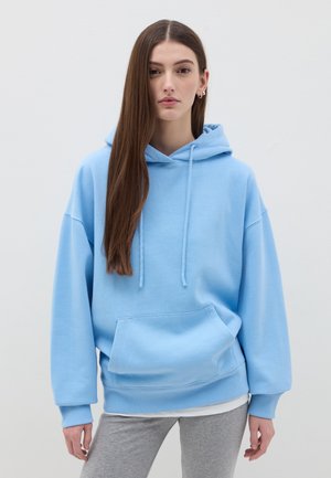 Light blue oversized hoodie with a front pocket, drawstring hood, ribbed cuffs, and a soft texture, paired with gray sweatpants.