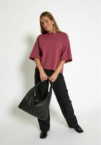 Oversized maroon top with half sleeves, paired with black trousers and a slouchy black leather bag. Model holds the bag at her side.