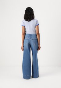 Camiseta de rayas de manga corta con detalles azules, combinada con jeans de mezclilla de pierna ancha en un azul claro que cuentan con bolsillos traseros y un acabado desgastado.