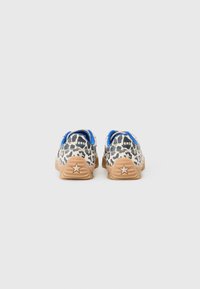 Sneakers med leopardprint, der har en beige bund, blå accenter og gummisåler med et stjerne-design på hælen.