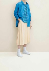 Camicia in denim blu con bottoni, t-shirt a righe blu e bianche, gonna midi plissettata pesca, sneakers bianche e calzini alla caviglia.