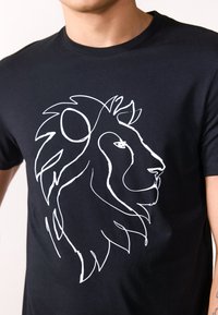 Zwarte katoenen T-shirt met een grote grafische afbeelding van een witte leeuwenkop op de voorkant, met gedetailleerde lijnen en een gestileerde manen.