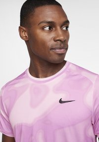 Camiseta deportiva rosa con un patrón de olas en degradado, cuello redondo, mangas cortas y logo negro de Nike en el pecho. Tejido ligero.