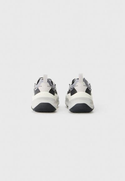 Zapatillas texturizadas en gris y negro con una gruesa suela blanca, que cuentan con una lengüeta en la parte posterior y acentos en contraste en la parte superior.