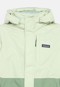 Svetlozelená nepremokavá bunda s kontrastnou tmavozelenou dolnou časťou, zipsom na hrudnej vrecku a nastaviteľnou kapucňou. Obsahuje logo Patagonia.