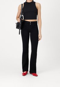 Top corto negro, pantalones vaqueros acampanados de cintura alta en negro, zapatos rojos y un pequeño bolso negro. Texturas suaves, hardware mínimo.