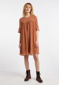 Roodbruine bloemenjurk met korte gerimpelde mouwen, geplooide details bij de borst en een vloeiende silhouette. Gestyled met bruin veterlaarzen.