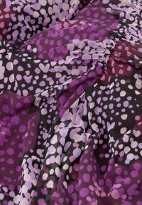 Doorzichtig materiaal met een kleurrijk stippenpatroon in tinten paars en roze op een zwarte achtergrond, met geplooide textuurdetails.