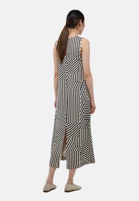 Robe longue sans manches avec des motifs géométriques noir et blanc, présentant des rayures verticales et horizontales, avec une fente dans le dos et une coupe décontractée.