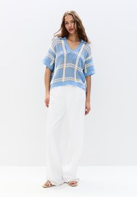 Lyseblå strikket pullover med V-udskæring, korte ærmer og ternet mønster i creme. Sæt sammen med løse hvide bukser og sandaler.