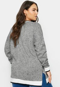 Cardigan grigio a maglia con maniche lunghe, fessure laterali e dettagli bianchi ai polsini e all'orlo. Tessuto testurizzato con una vestibilità comoda.