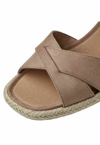 Sandale en daim beige avec des brides croisées et une semelle en corde tissée, montrant les détails de face et de côté.