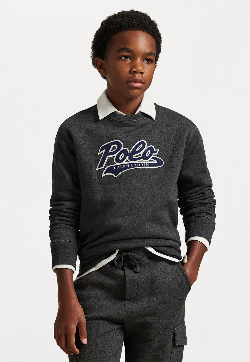 Tumši pelēks džemperis ar apaļu kaklu, ar zilu un baltu 'Polo Ralph Lauren' logo. Apvienots ar atbilstošām pelēkām biksēm un baltu apkakles detaļu.