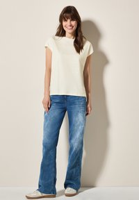 Creme kortærmet t-shirt med rund halsudskæring, parret med lyse, flagrende jeans. Minimalistisk design; blød stoftekstur.