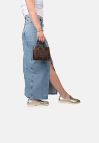Denim maxirok met een uitsparing aan de voorkant, gecombineerd met metallic gouden instappers. Kleine handtas met luipaardprint in één hand.
