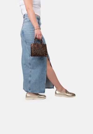 Denim maxi skirt with front slit, paired with metallic gold slip-on shoes. Small leopard print handbag held in one hand.