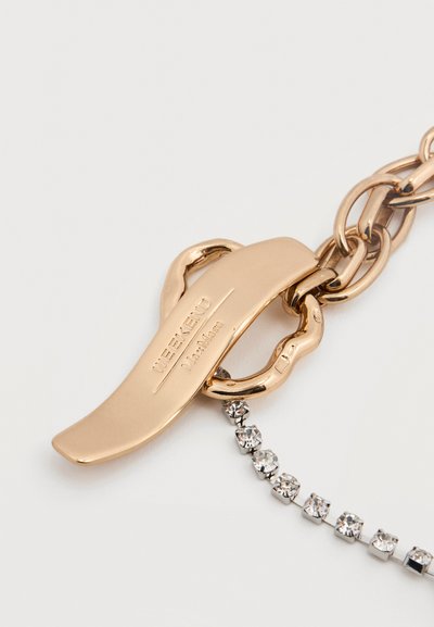 Μπρελόκ από μέταλλο με επίχρυσο τόνο, με λείο οβάλ κλιπ και σειρά από μικρές καθαρές στρας, που ενισχύουν τη λάμψη και την κομψότητά του.