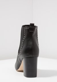 Černá kotníková bota z kůže se stříbrnými cvočky, elastickými bočními panely a blokovým podpatkem. Hladká textura s kulatou špičkou.