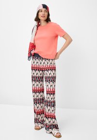 Coral short-sleeve top paired with patterned wide-leg trousers featuring blocks of red, pink, and navy geometric designs. Flat sandals complete the look.