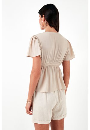 Top plisado beige con mangas cortas abullonadas y cintura fruncida, combinado con pantalones cortos beige claros. Tejido suave y corte relajado.