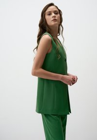 Top verde senza maniche con scollatura a V e dettagli di bottoni, abbinato a pantaloni verdi coordinati. Tessuto liscio e strutturato; design semplice e moderno.