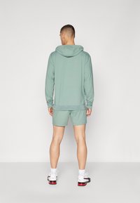 Hoodie atlético de color verde claro con capucha y pantalones cortos a juego, fabricado con un tejido suave, que presenta un ajuste relajado y un diseño minimalista.