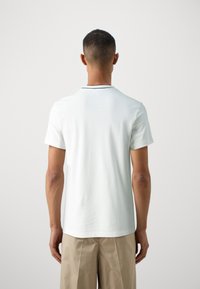 T-shirt bianco a maniche corte con colletto rotondo, caratterizzato da un bordo nero a contrasto lungo il colletto. Tessuto di cotone morbido.