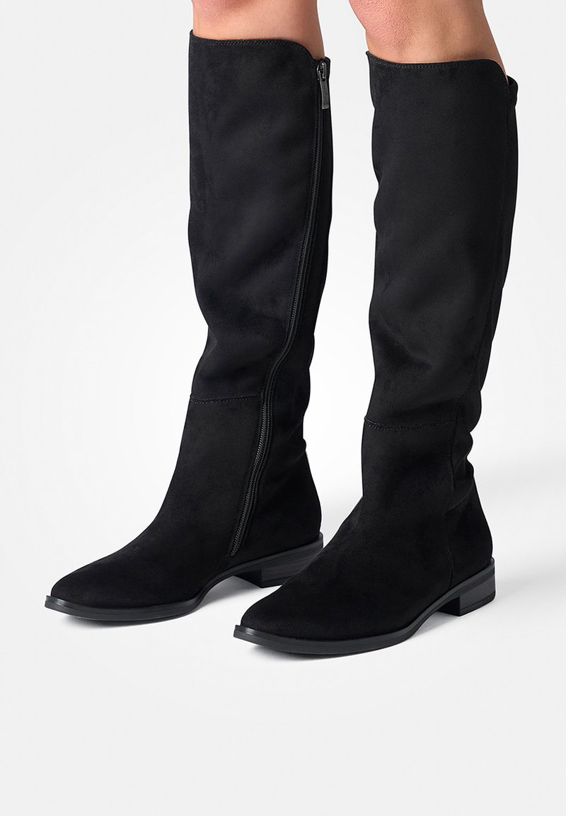 Botas negras hasta la rodilla, hechas de suave ante, con suela plana y cremallera lateral para facilitar su uso. El diseño presenta un acabado suave y líneas simples.