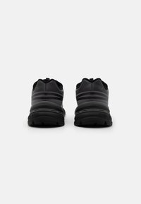 Baskets de sport noires avec un dessus lisse orné de rayures, semelles rembourrées et semelle texturée pour une meilleure adhérence. Design minimaliste avec des languettes de traction.