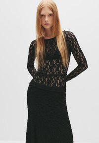 Outfit a strati neri composto da una top in pizzo a maniche lunghe e una gonna nera con texture. Il pizzo presenta un motivo floreale e un aspetto trasparente.