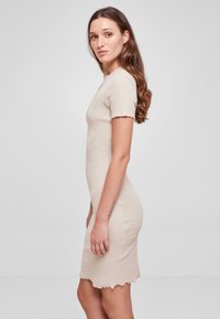 Robe beige à rayures avec des manches courtes, design ajusté et ourlet en dentelle. La texture semble douce et légèrement extensible.