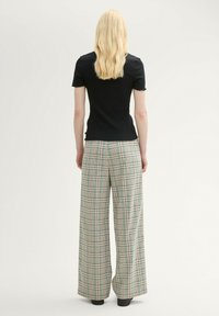 Svart randig kortärmad topp i kombination med vida rutiga byxor som har gröna och blå linjer på en beige bakgrund.