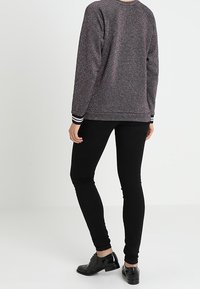 Suéter gris texturizado con motas multicolores, pantalones negros ajustados y zapatos negros brillantes con detalles brogue. Puños a rayas en blanco y negro.