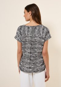 Haut à manches courtes noir et blanc à rayures zébrées avec un col rond et une couture dans le dos, fabriqué à partir d'un tissu léger.