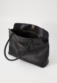 Sac fourre-tout en cuir noir avec deux poignées, matériel doré et poche zippée intérieure. Dispose d'un compartiment principal spacieux. Texture lisse.