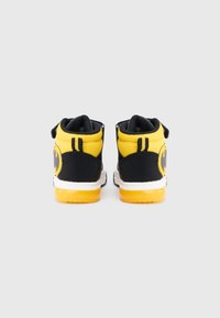 Sneaker alte nere e gialle con tomaia in rete, suola in gomma e un evidente logo di Batman sul tallone.