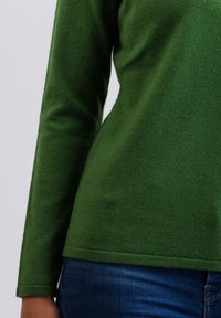 Zelený dlouhý rukáv top z měkké tkaniny s přiléhavým střihem, s kulatým výstřihem a lemem, v kombinaci s tmavě modrými džínami.