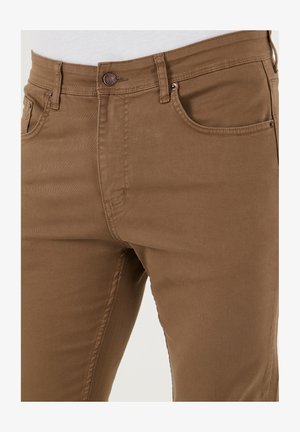 Braune Baumwollhosen mit schmaler Passform, fünf Taschen und Metallknopfdetails am Bund. Gleiche Textur, strapazierfähiger Stoff.