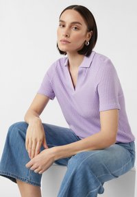 Lavendelfarbenes Kurzarm-Polohemd mit strukturiertem Strickdesign und V-Ausschnitt, kombiniert mit weit geschnittenen blauen Jeans.