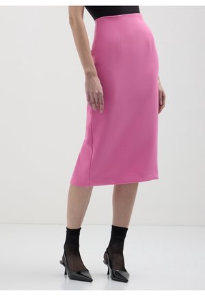 Personne portant une jupe midi rose vif, des chaussettes en résille noires et des escarpins noirs à bouts pointus sur un fond blanc uni.