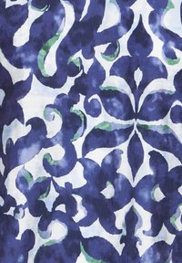Un motif damas floral bleu et blanc avec de subtiles accents verts sur le tissu, présentant des formes de feuilles et de pétales symétriques et fluides.