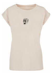 Helles beige T-Shirt mit kurzen Ärmeln aus weicher Baumwolle. Mit einem schwarzen Totenkopf-Graphic, das auf der Brust zentriert ist. Lässiger Schnitt mit hochgerollten Ärmeln.