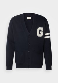 Mörkblå cardigan med v-ringad hals, vitt "G"-logotyp och två ränder på vänster ärm, med knäppning fram och två framfickor.
