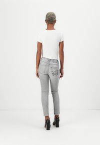 Grå skinny jeans med en baklommepregning som har en brodert detalj, kombinert med en hvit tettsittende topp og svarte høyhælte sko.