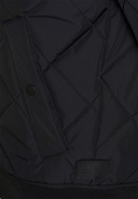 Czarna pikowana kurtka o teksturowanej powierzchni, z kieszenią na zatrzask, ściągaczem na dole oraz tłoczonym naszywką z logo.