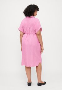 Ροζ και λευκή ριγέ midi φόρεμα με κοντά μανίκια, τσιτωμένη μέση και πλαϊνές σχισμές. Λείος, ελαφρύς ύφασμα. Μαύρες επίπεδες παπούτσια.