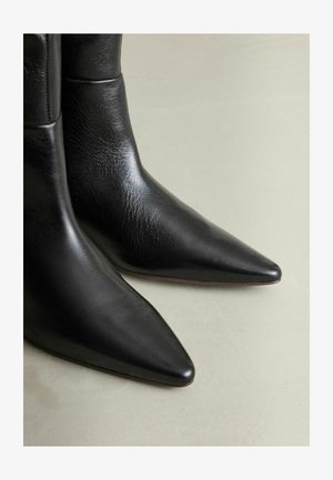 Černé kožené kotníkové boty s špičatou špičkou, hladkým povrchem a elegantním designem. Viditelné švy v horní části.